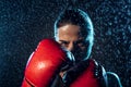 Concentrated boxer in red boxing gloves standing under water drops on black.