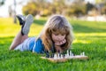 Concentrated boy developing chess strategy, playing chess board game. Cute little boy playing chess, laying on grass in