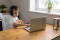 Concentrated boy in headphones plays ukulele guitar and watches online course on laptop while studying at home. Online training,