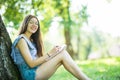 Side view of concentrated brunette woman in eyeglasses sitting near the tree in park and writing something on notebook