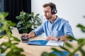 Concentrated businessman in headphones working with documents and laptop in office Royalty Free Stock Photo