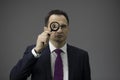 Concentrated businessman looking through loupe, isolated grey background