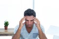 Man holding temples with fingers while working at desk in home office with laptop, plant, blinds Royalty Free Stock Photo