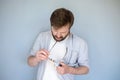 Concentrated Caucasian man cleans glasses from dust and dirt, wiping them with his shirt. Gray background.