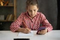 Concentrated child girl doing homework at the her room, student learning at home using smartphone for remote education Royalty Free Stock Photo