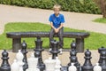 Concentrated child, thinking about his next move, sitting on a wooden bench during an outdoor chess game using life sized pieces Royalty Free Stock Photo