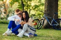 Concentrated couple is sitting on a grass in the park and using smartphone. A man is pointing a finger and showing something on