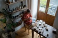 Concentrated creative ceramic woman sits at table and covers natural clay dishes with white lacquer