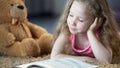 Concentrated cute girl reading book, lying on carpet, preschool education Royalty Free Stock Photo