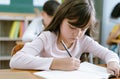 Concentrated cute schoolgirl sits table writing or drawing on textbook in classroom at the elementary school. Student girl doing Royalty Free Stock Photo