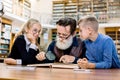 Concentrated elderly man teacher professor and his two little clever cute students reading book together. Grandfather Royalty Free Stock Photo