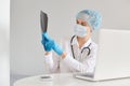 Concentrated female doctor wearing medical cap, surgical mask, rubber gloves and gown, using notebook for working, having video Royalty Free Stock Photo