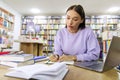 Concentrated female student studying with books and laptop in library, preparing for evaluation examination, tests or Royalty Free Stock Photo
