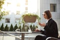 Concentrated freelance woman in business casual clothes holds a mobile phone and types on laptop keyboard, works remotely sitting