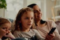 Concentrated girl holding remote control watching television with mother and sister at home