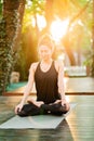 Concentrated girl sitting in lotus pose and meditating or praying. Young woman practicing yoga alone on wooden deck in Royalty Free Stock Photo