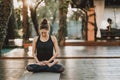 Concentrated girl sitting in lotus pose and meditating or praying. Young woman practicing yoga alone on wooden deck in Royalty Free Stock Photo