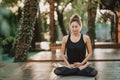 Concentrated girl sitting in lotus pose and meditating or praying. Young woman practicing yoga alone on wooden deck in Royalty Free Stock Photo