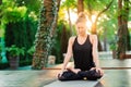 Concentrated girl sitting in lotus pose and meditating or praying. Young woman practicing yoga alone on wooden deck in Royalty Free Stock Photo