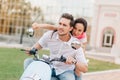 Concentrated guy with beard driving scooter in warm autumn day. Gorgeous brunette woman with happy face expression