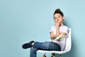 Concentrated schoolboy sits on chair holding dollars and touching chin with hand thinking how to earn more. Portrait isolated on