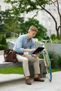 Concentrated, handsome young businessman sitting on bench outside office with bike and working online on tablet Royalty Free Stock Photo