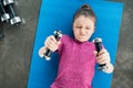 Concentrated little girl lying on mat and exercising with dumbbells Royalty Free Stock Photo