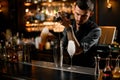 Concentrated male bartender pouring a liqour from the jigger to a professional steel shaker