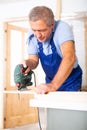 Concentrated male builder in uniform using a jigsaw machine on wooden plank at the apartment Royalty Free Stock Photo