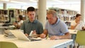 Focused male coworkers discussing remote job and searching in Internet in the library