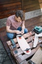 Concentrated man assembling skateboard truck and deck while sitting outdoor