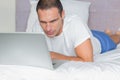 Concentrated man lying on bed using his laptop