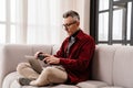 Concentrated man using mobile phone while working with laptop on couch Royalty Free Stock Photo