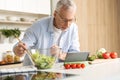 Concentrated mature man cooking salad using tablet