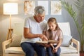 Concentrated mature man and little girl reading book with focused expression grandfather teaching his granddaughter sitting on Royalty Free Stock Photo