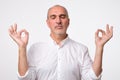 Concentrated mature man in white shirt tries to relax, daydreams, keeps fingers together. Meditation and relax concept. Royalty Free Stock Photo