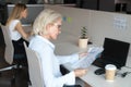 Focused middle-aged woman reading financial report at shared office desk