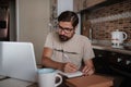 Concentrated millennial hipster guy wearing glasses, listening to favorite music while planning workday Royalty Free Stock Photo