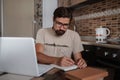 Concentrated millennial hipster guy wearing glasses, listening to favorite music while planning workday Royalty Free Stock Photo
