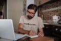 Concentrated millennial hipster guy wearing glasses, listening to favorite music while planning workday Royalty Free Stock Photo