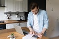 Concentrated millennial man planning monthly budget in kitchen. Royalty Free Stock Photo