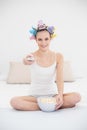 Concentrated natural brown haired woman in hair curlers watching tv while eating popcorn