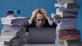 Concentrated office worker businessman works on laptop among piles of paperwork