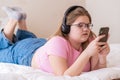 Concentrated overweight teenage girl in headphones lying on bed watching TikTok