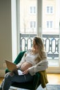 Concentrated preggers lady with bare tummy sitting on armchair and looking at monitor of laptop, working from home. Royalty Free Stock Photo