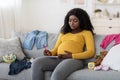 Concentrated pregnant woman sitting on sofa with notebook and pen