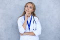 Concentrated pretty doctor with hanf on chin posing over grey background