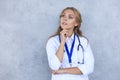 Concentrated pretty doctor with hanf on chin posing over grey background