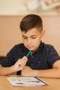 Concentrated schoolboy sitting at desk and writing in exercise book Royalty Free Stock Photo