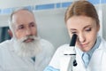 Concentrated scientists in uniform working together with microscope